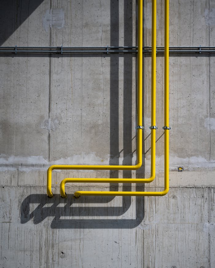 who-we-are Vertical yellow pipes casting shadows on a rugged concrete wall in Berlin.