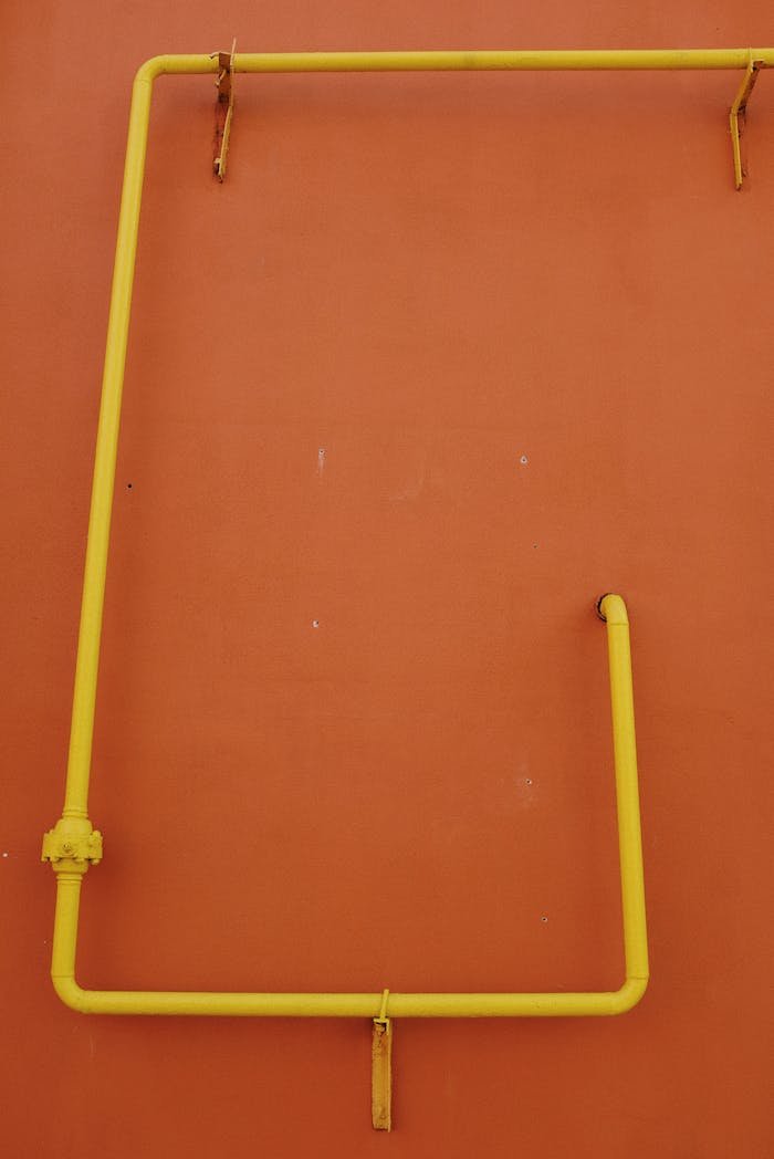 Abstract view of yellow pipes contrasting against a vivid orange wall.
